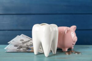 Large model tooth next to a piggy bank and money on a blue surface